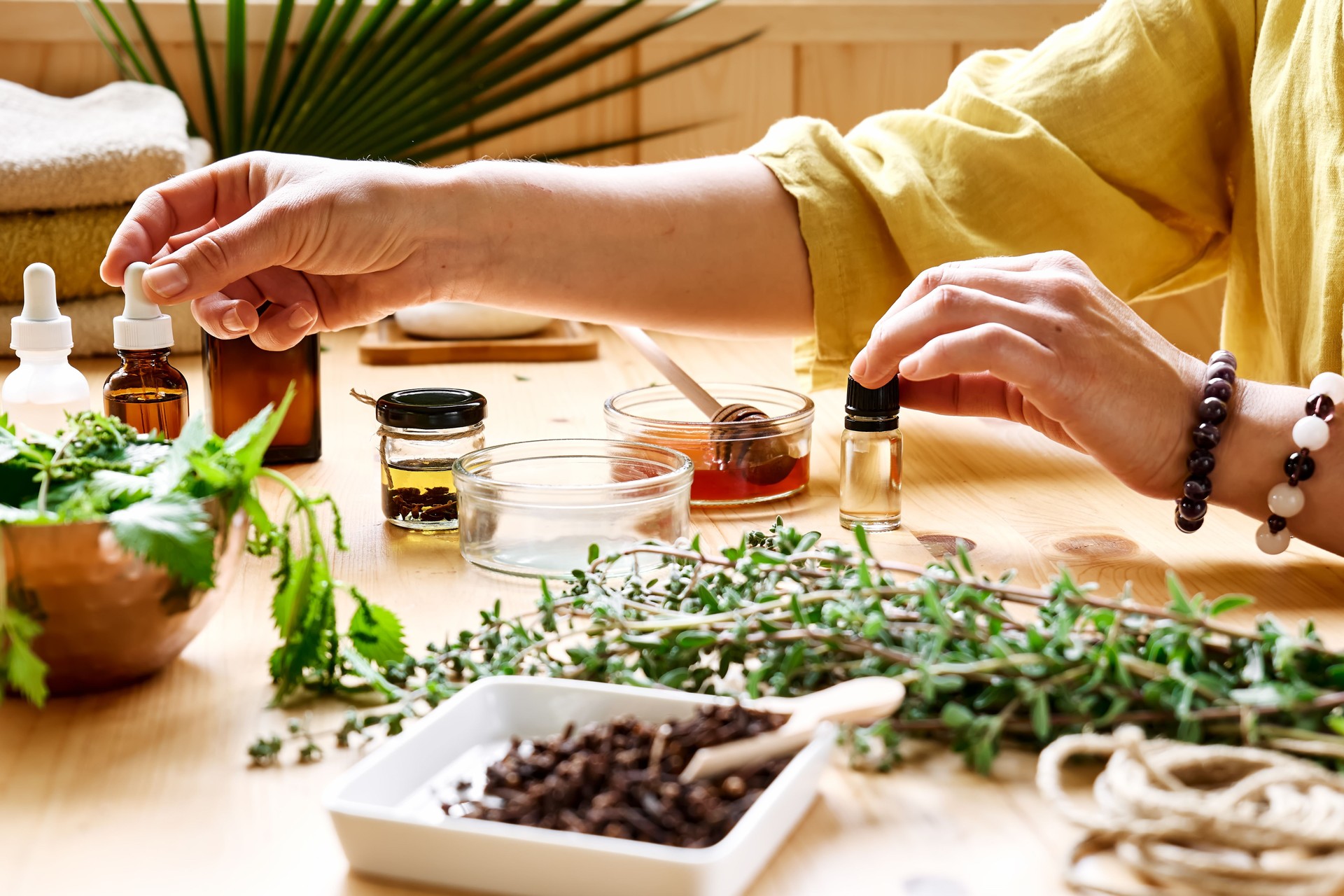 Woman prepares aromatherapy session at the table with essential oil diffuser medical herbs, different types of oils and essences. Aromatherapy and alternative medicine concept. Natural remedies.